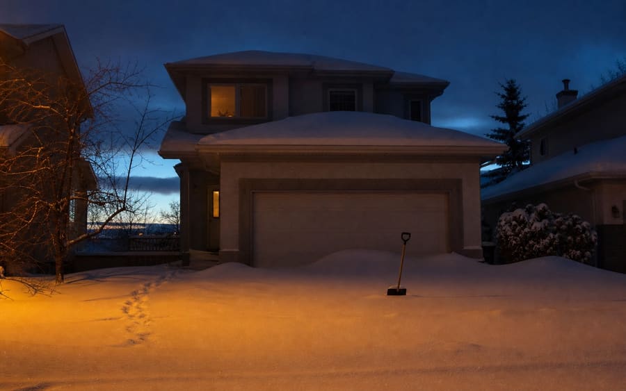 A Calgary driveway, front walk and sidewalk buried under 18 cm of overnight snow, a shovel standing upright in the drift.